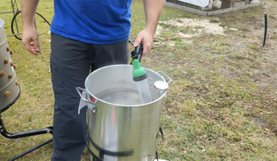 man using a hose to add water to a chicken scalder outside